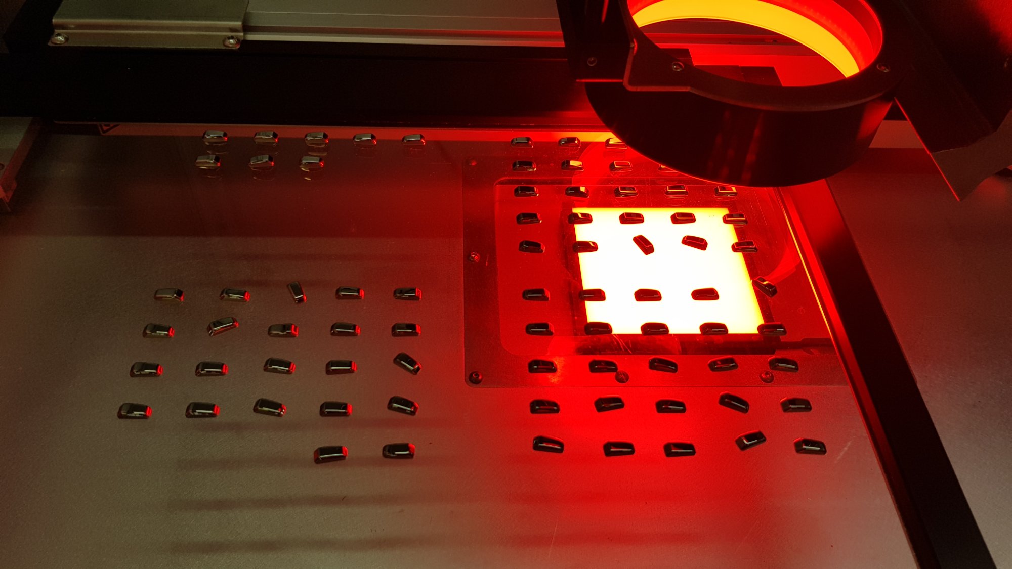 Watch crown laser engraving — production setup with fixture and red LED illumination